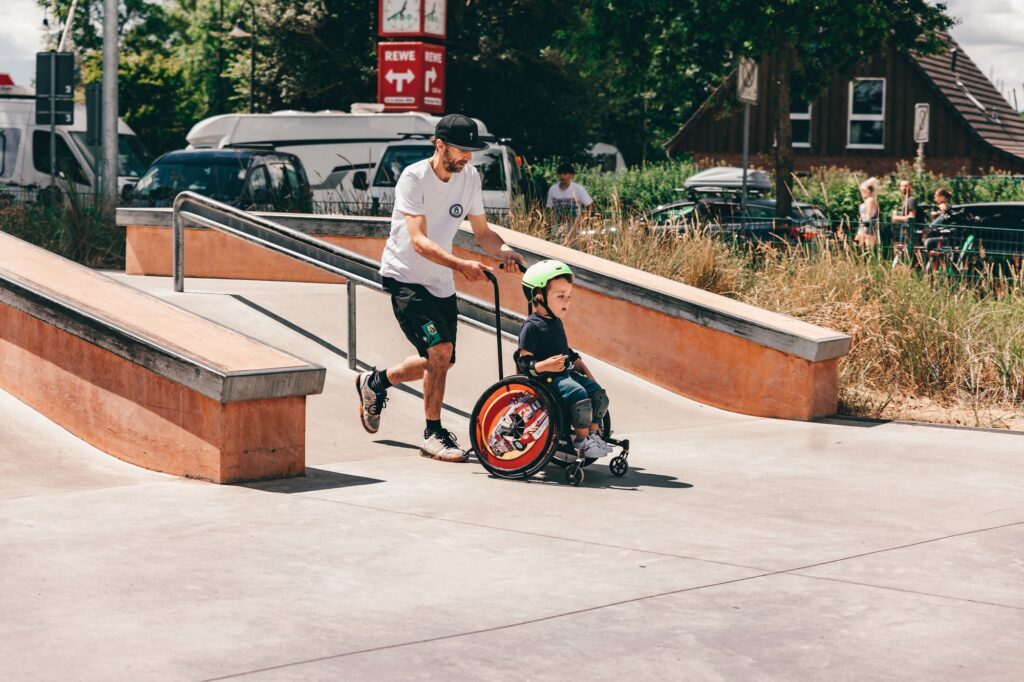 Assistent schiebt einen Jungen im Rollstuhl durch den Skatepark