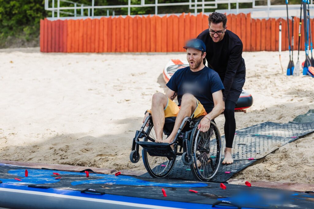 Assistent hilft einem Rollstuhlfahrer aufs Stand-up-Paddle-Board