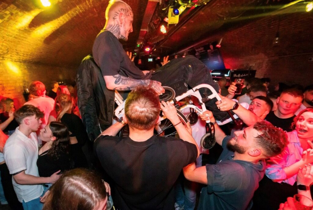 Mann im Rollstuhl wird auf einer Party von Freunden in die Luft gehoben