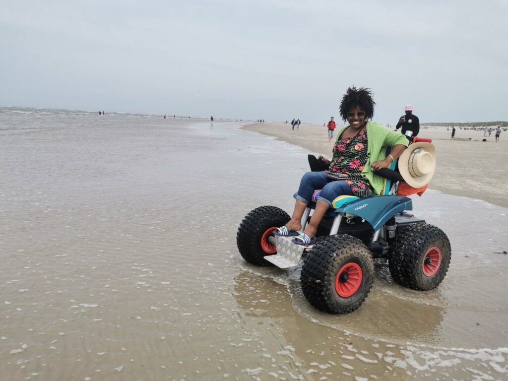 Lachende Frau im geländegängigen Strandrollstuhl am Meer